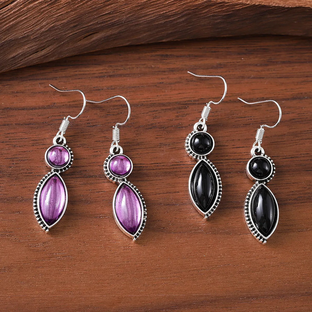 Close-up of vintage black and purple geometric drop earrings with a circular pendant on a long chain.