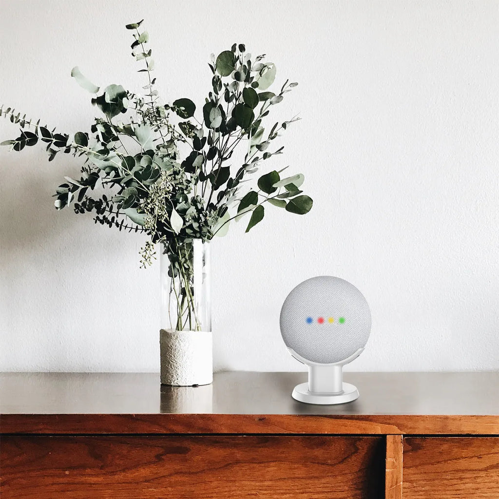 Black plastic stand holding Google Home Mini speaker on wooden desk