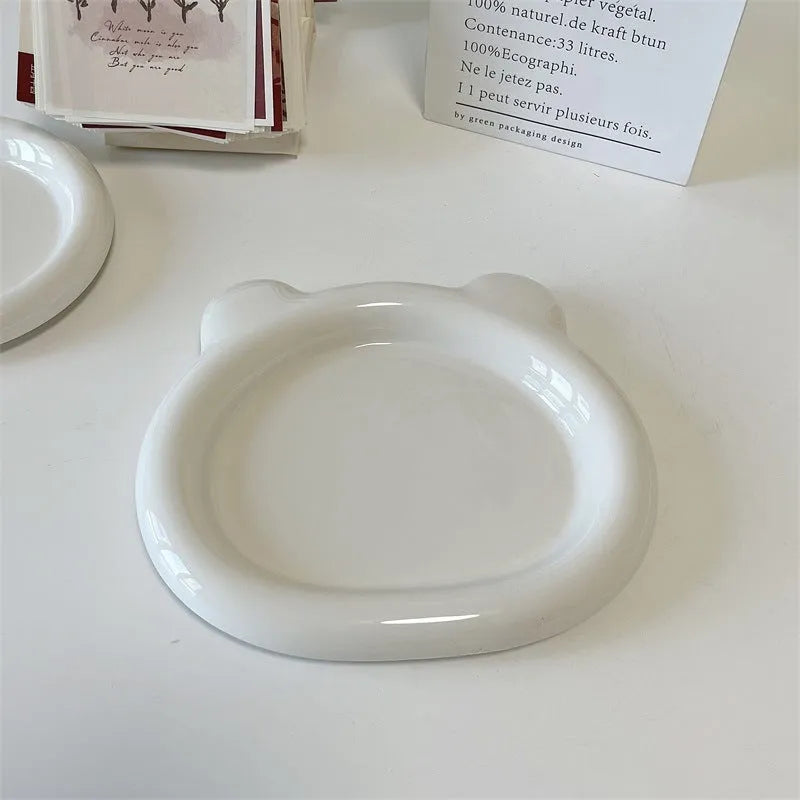 White ceramic plate with cartoon bear doodle design, shown next to round toot design plate, both microwave safe.