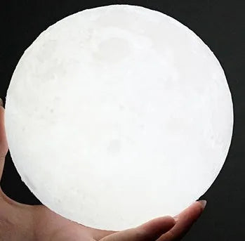 3D printed white moon lamp on a wooden holder, showing detailed lunar surface and a glowing yellow light.