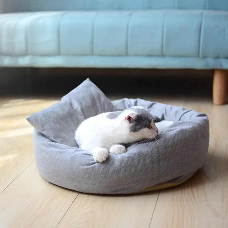 Grey round plush pet bed with raised edge and pillow, shown on a non-slip base.