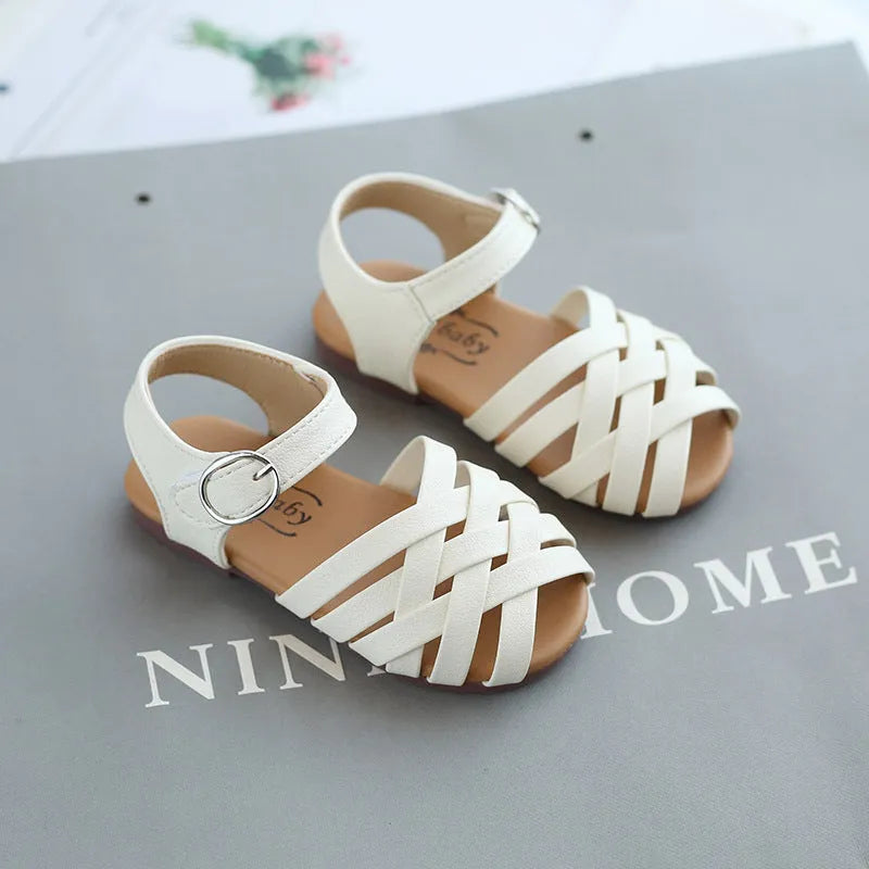 Kids buckle-toe soft sole woven sandals in white, black, and pink on a light background