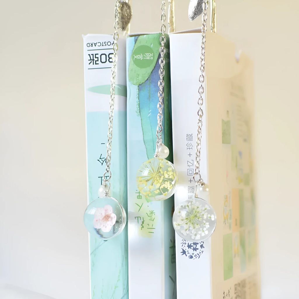 Flat metal bookmark with dried flower inside, showing 12cm length, on an open book.