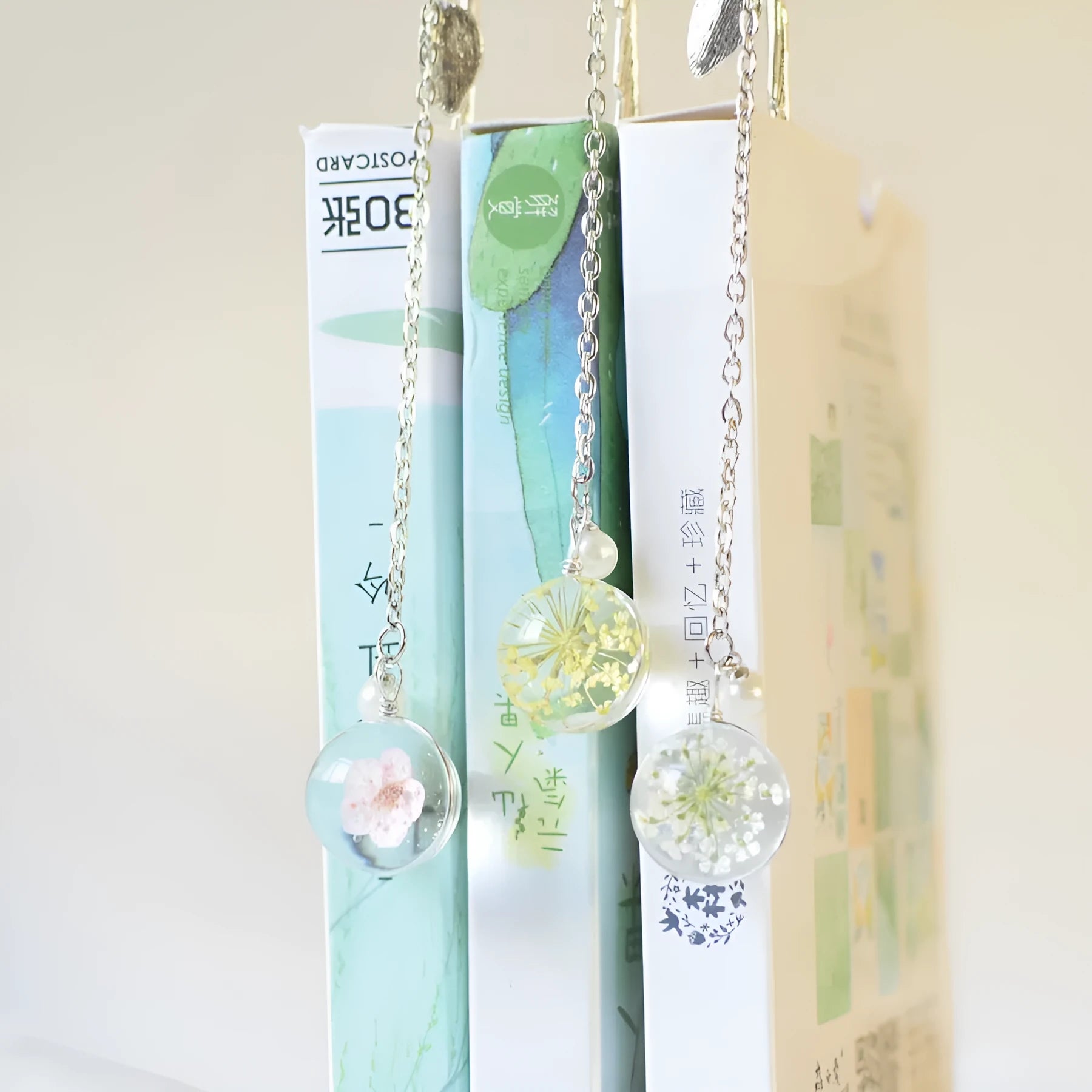 Flat metal bookmark with dried flower inside, showing 12cm length, on an open book.