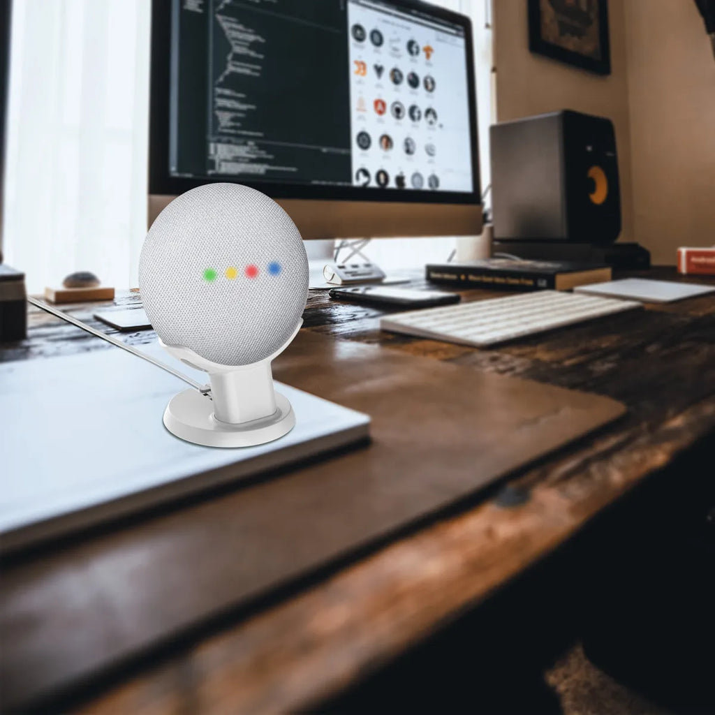 Black plastic stand holding Google Home Mini speaker on wooden desk