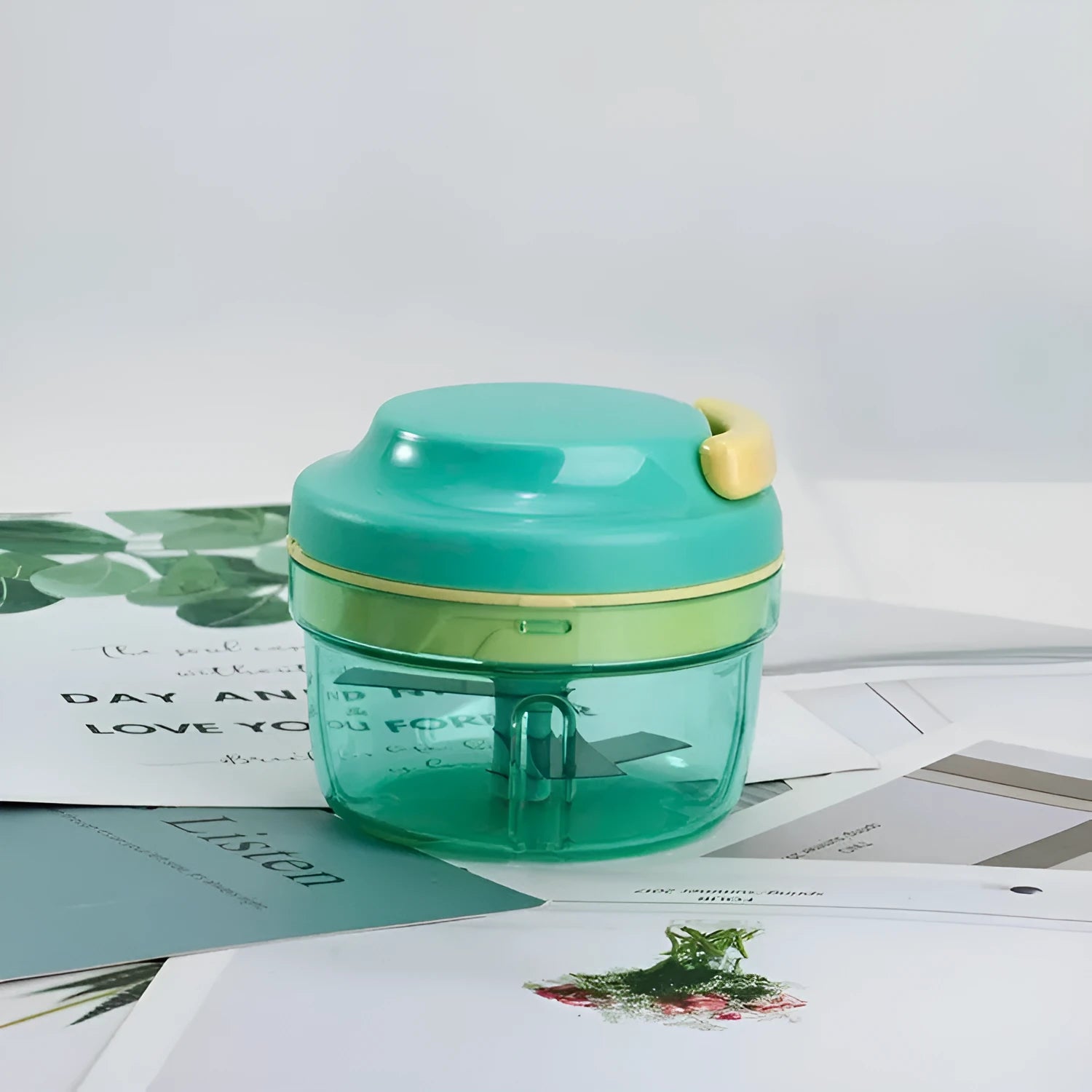 Green manual hand-pulled food grinder with transparent container and stainless steel blade for baby food and herbs.