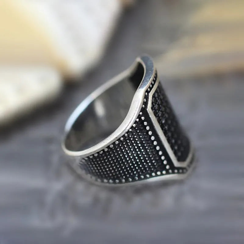 Close-up of a black alloy ring with a zircon stone set in a copper inlay pattern on a person's finger.
