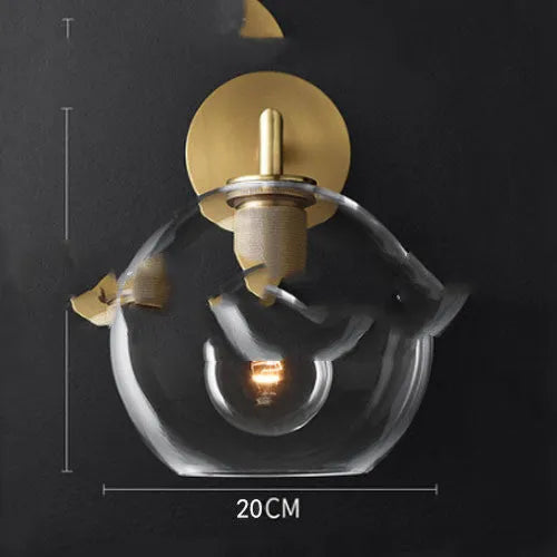 Gold bronze or black wall lamp with triangular transparent glass shade and wrought iron frame for bedside or hallway use