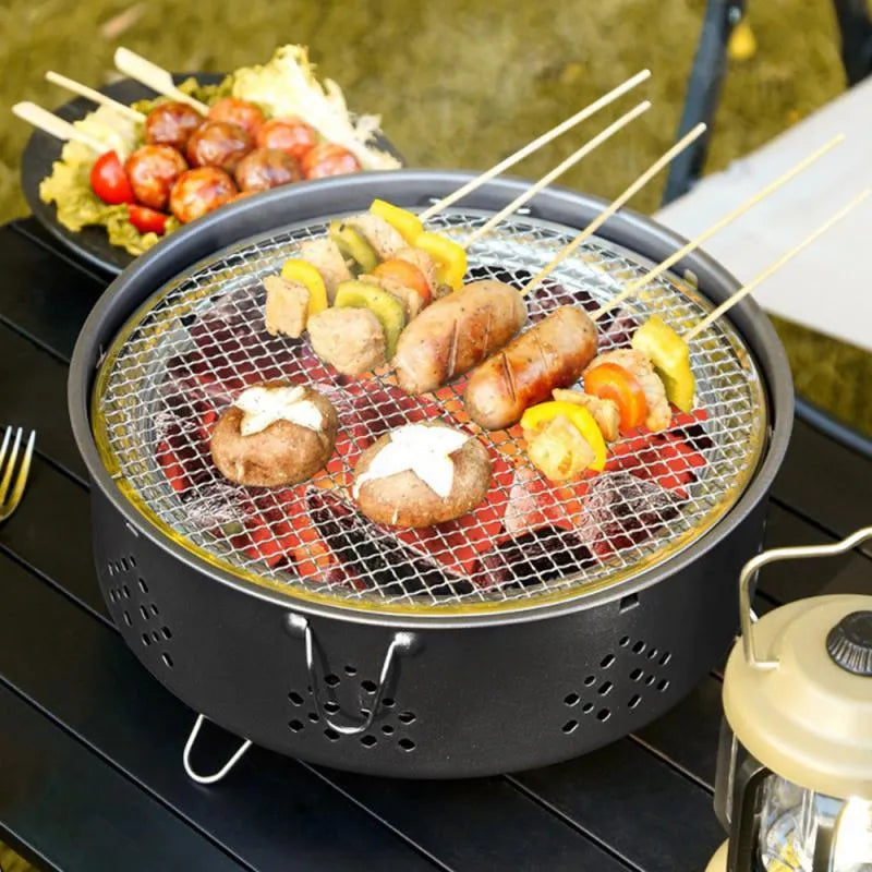 Portable stainless steel barbecue grill with detachable parts on a grassy outdoor surface.