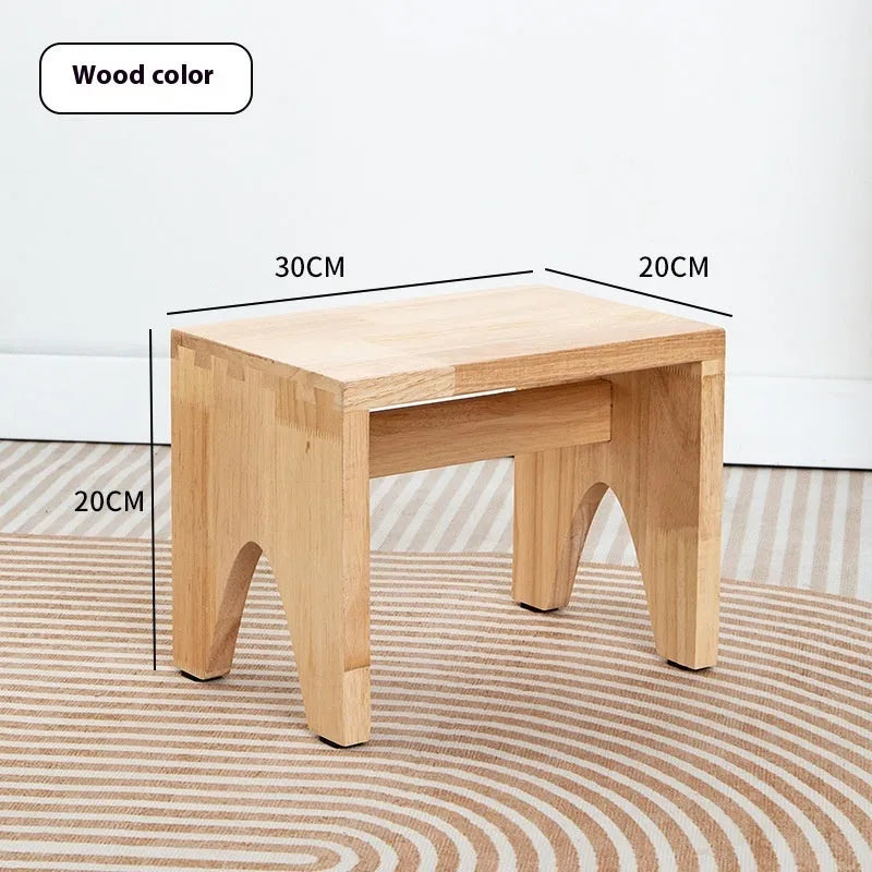 Distressed solid wood shoe changing stool with bracket legs in a living room setting.