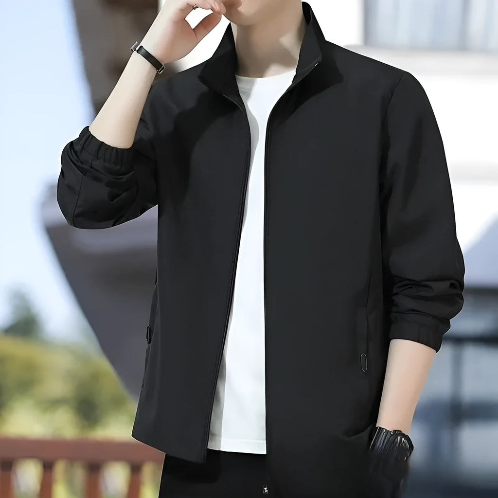 Man wearing a loose-fit black casual autumn jacket with a lapel and zippered pockets.