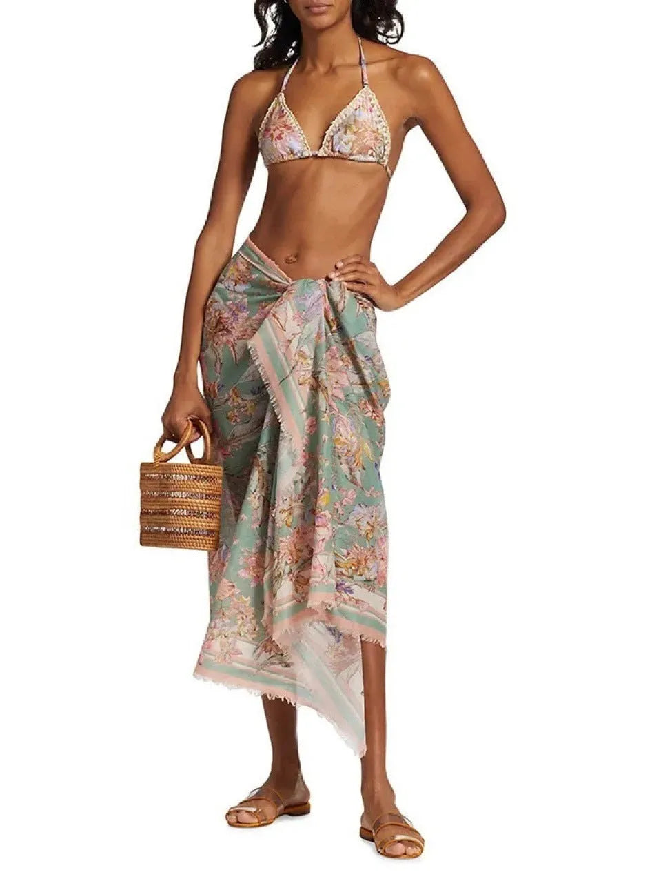 Women's creamy-white floral bikini swimsuit set with matching skirt on a beach background.