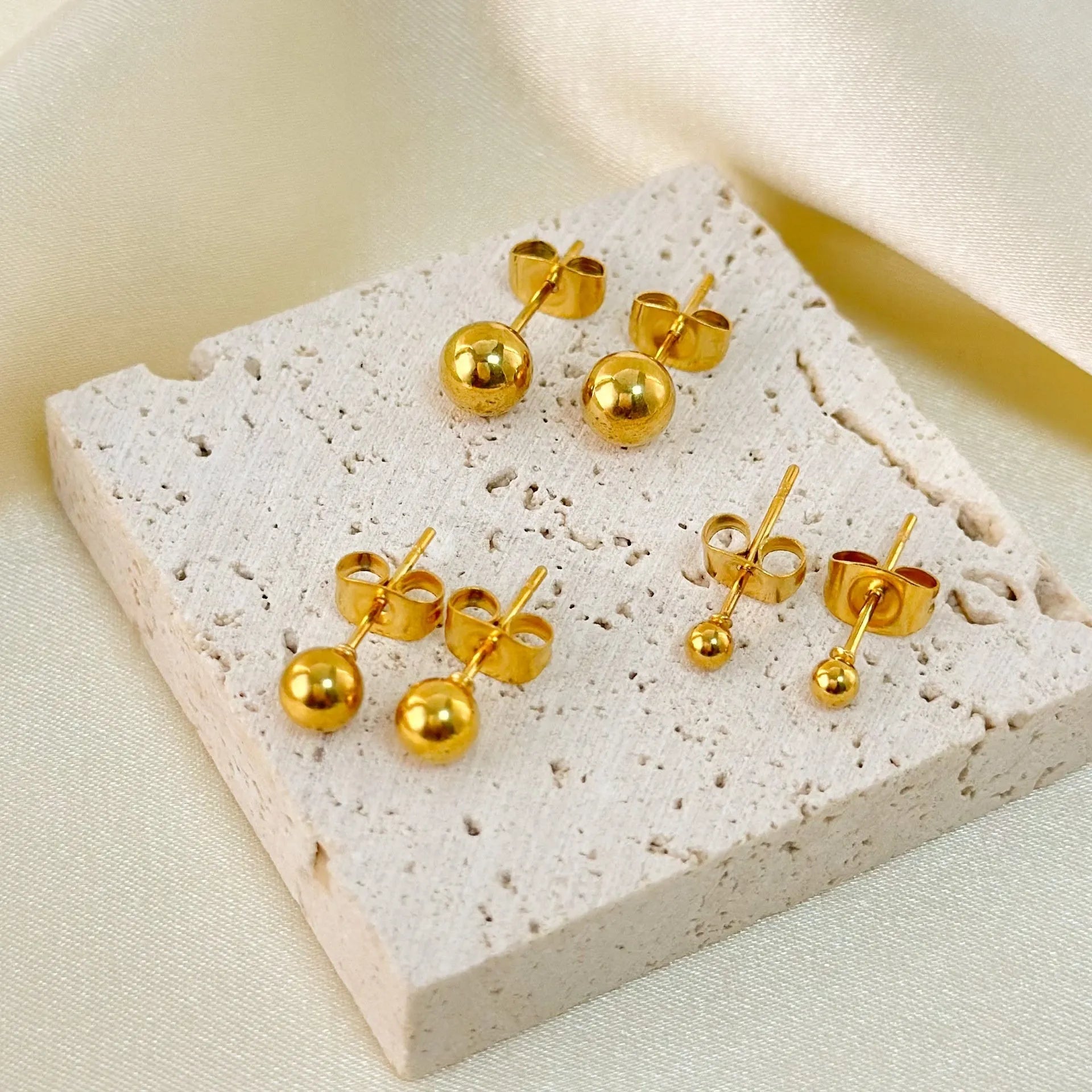 Simple gold-coloured stainless steel ball stud earrings in geometric design on a white background.