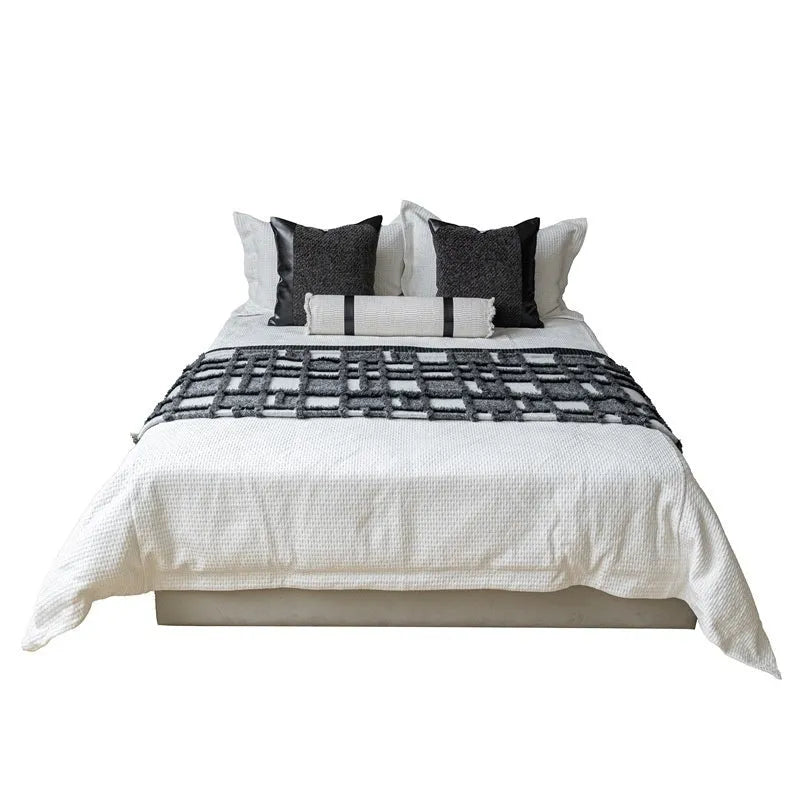 Modern grey and white plaid bed runner set with matching pillowcase and a brown leather round pillow on a bed.