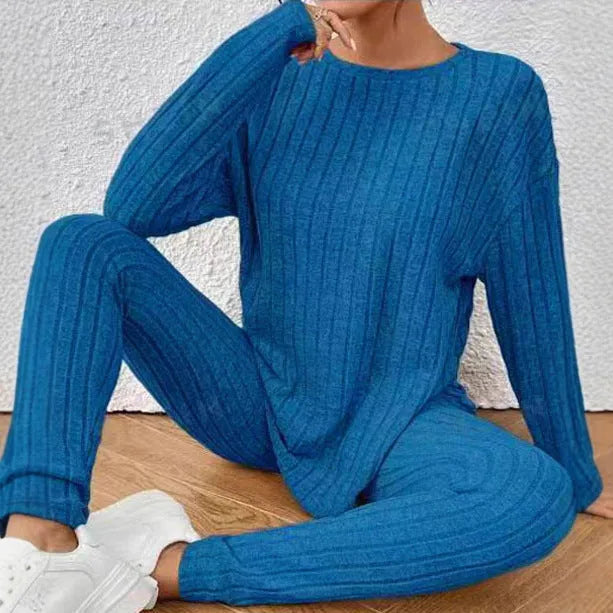 A woman wearing a black sunken stripe two-piece loungewear set, consisting of a regular-sleeve top and elasticated waist trousers.