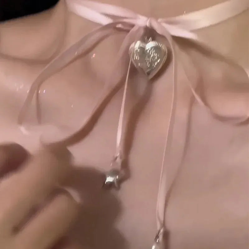 Close-up of a women's alloy fashion necklace with a love pendant and ribbon detail on a delicate clavicle chain.
