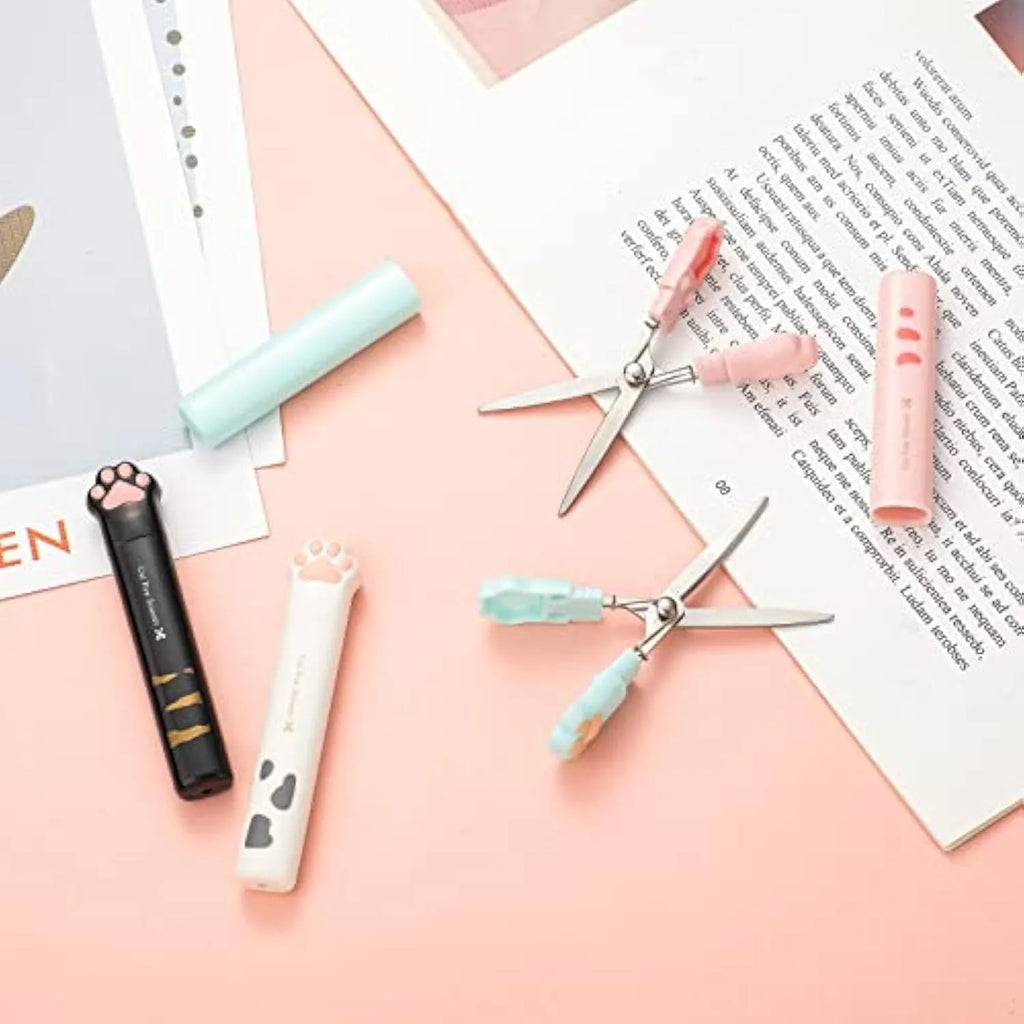 Set of four mini folding scissors with cat paw design in black, blue, pink, and white colours on a plain surface.