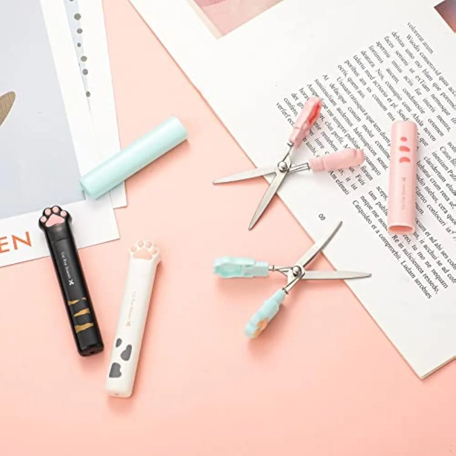 Set of four mini folding scissors with cat paw design in black, blue, pink, and white colours on a plain surface.