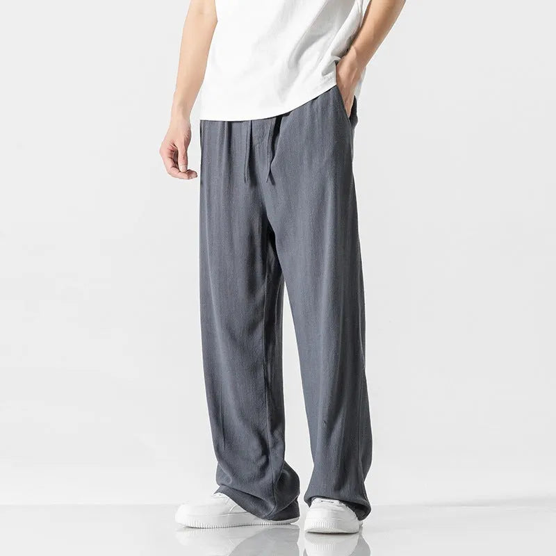 Man wearing beige straight-leg cropped bamboo fibre trousers with a drawstring waist on a summer day.