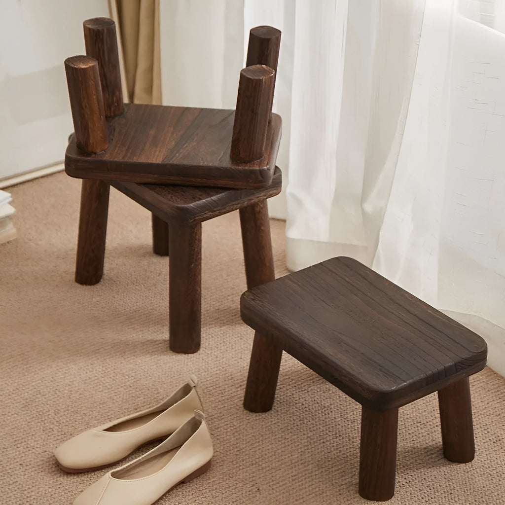 Distressed solid wood shoe changing stool with bracket legs in a living room setting.