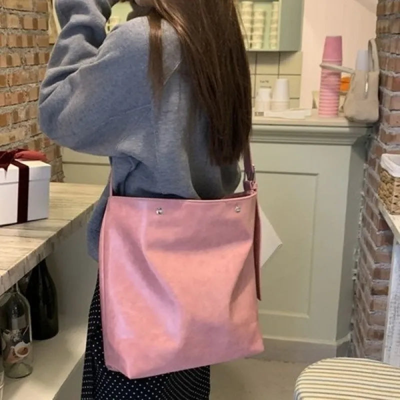 Corduroy one-shoulder messenger bag in pink on a table, showing adjustable strap and structured shape.