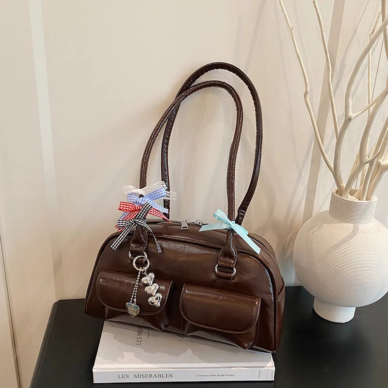 Retro-style brown PU leather women's pillow handbag with a one-shoulder strap, shown with a decorative ribbon pendant.