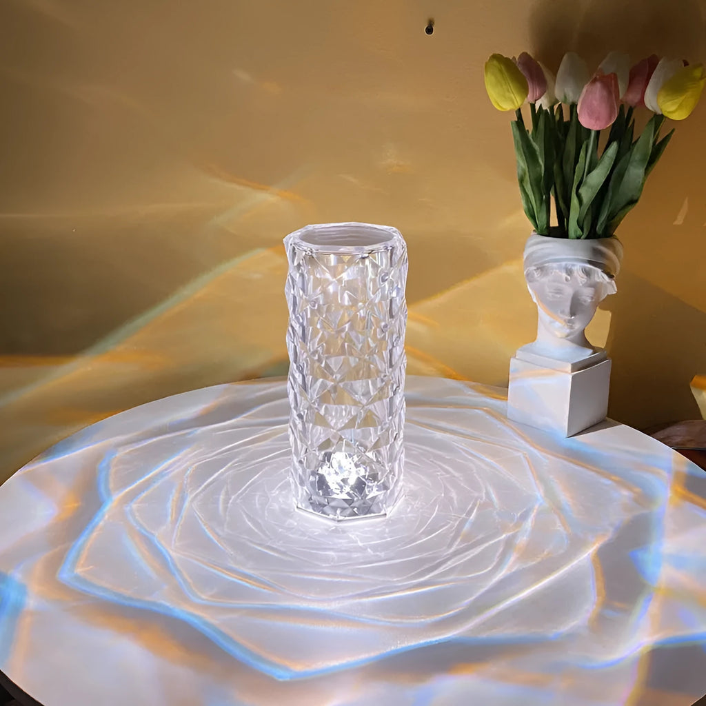 Clear acrylic crystal rose shaped LED table lamp with diamond-like facets on a table.