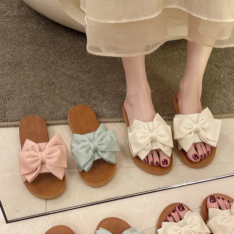 Women's beige slip-on cloth sandals with a bow on the upper and a soft flat rubber sole.