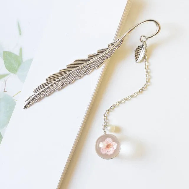 Flat metal bookmark with dried flower inside, showing 12cm length, on an open book.