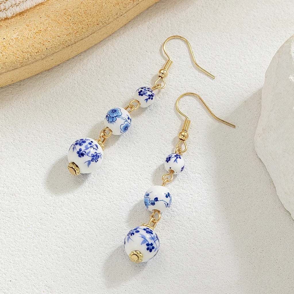 Long blue and white porcelain ceramic bead earrings with geometric alloy details on a white background.