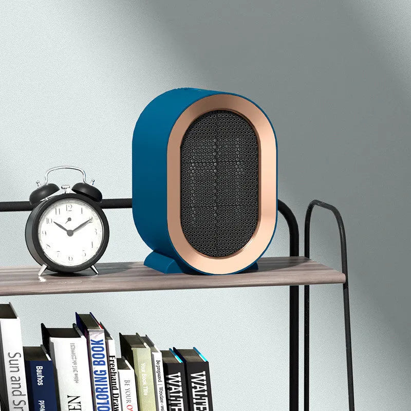 A compact black desktop electric fan heater with mechanical control dials on a wooden desk.