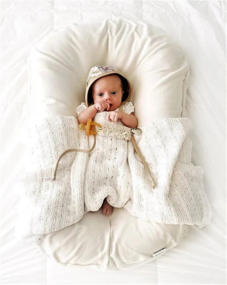 Beige portable baby nest cot crib for infants on a neutral background