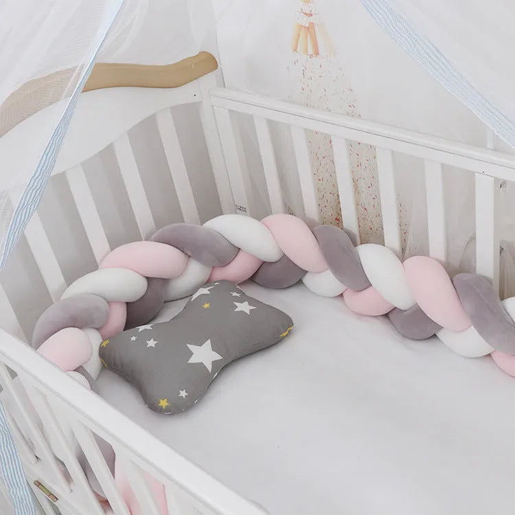 Close-up of a grey braid knot pillow cushion cot bumper fitted around white crib rails.