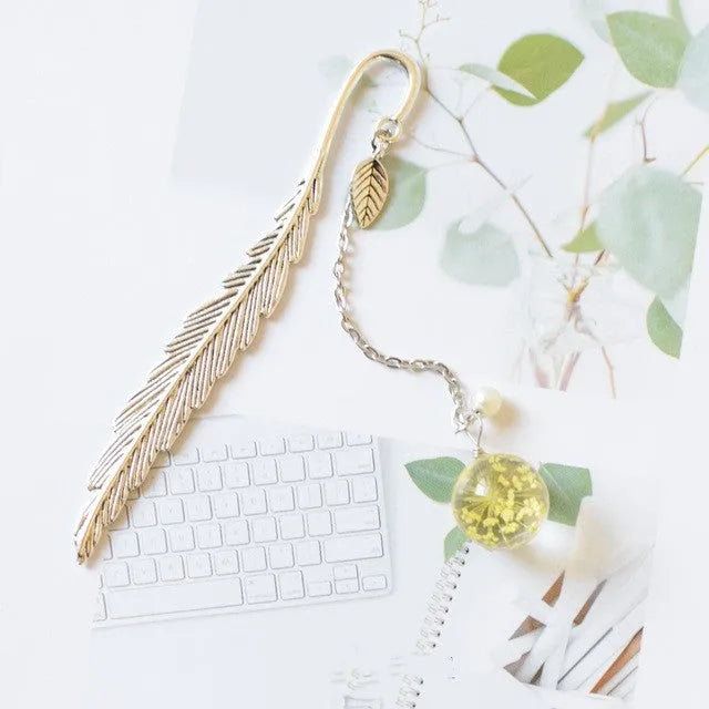 Flat metal bookmark with dried flower inside, showing 12cm length, on an open book.