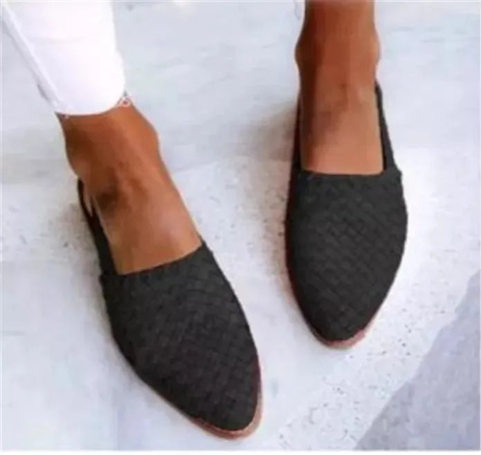 A pair of black baotou flat sandals with a buckle fastening and a pointed toe on a rubber sole.