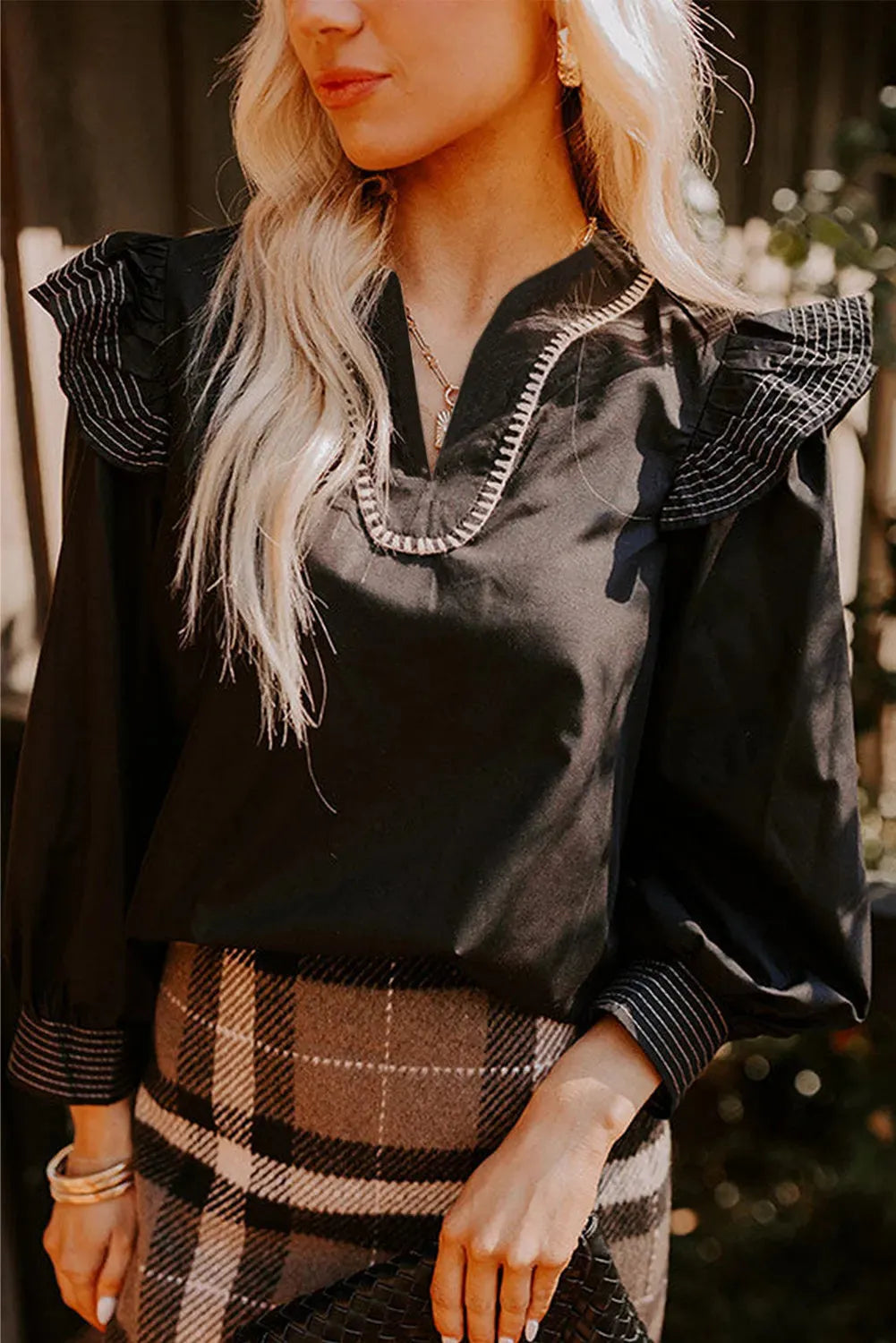 Black women's V-neck blouse with ruffle detailing on the long sleeves and contrast stitching.