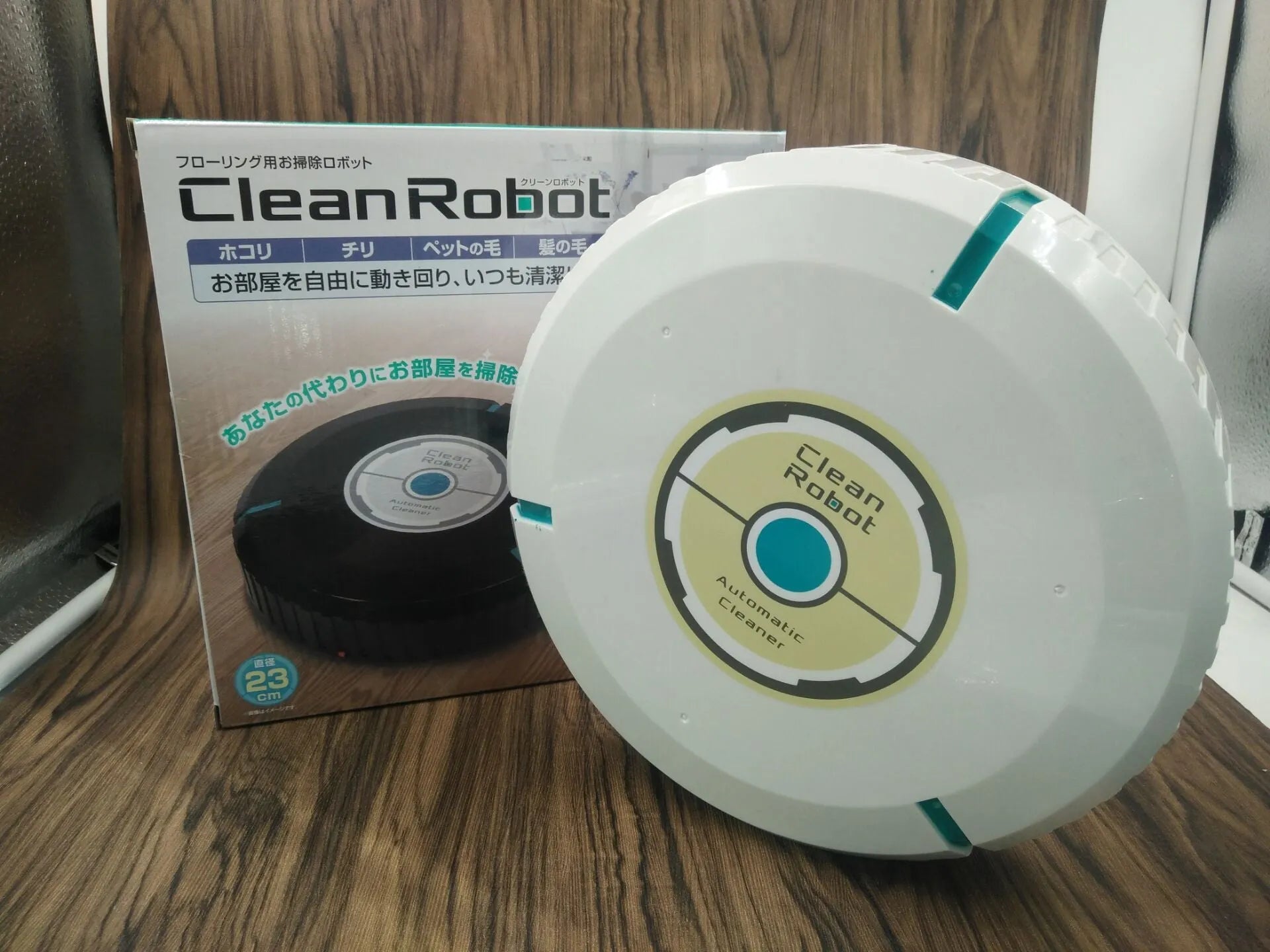 Black and white compact AC automatic sweeping robot vacuum cleaner on a wooden floor.