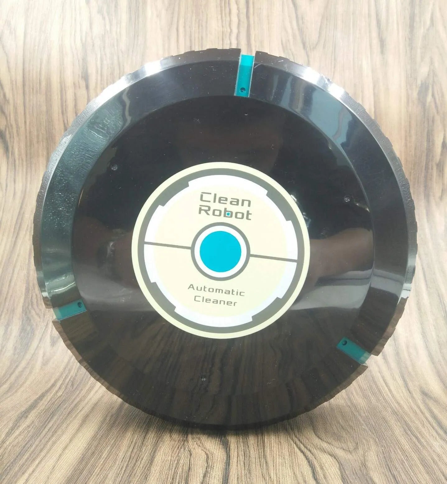 Black and white compact AC automatic sweeping robot vacuum cleaner on a wooden floor.