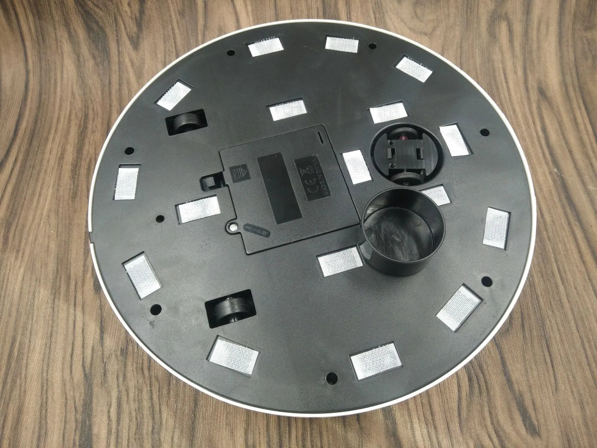 Black and white compact AC automatic sweeping robot vacuum cleaner on a wooden floor.