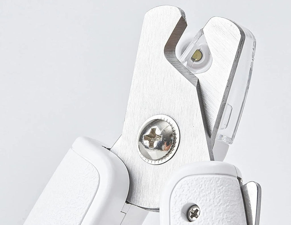White pet nail clippers with LED light and transparent anti-splash guard next to a nail file on a table