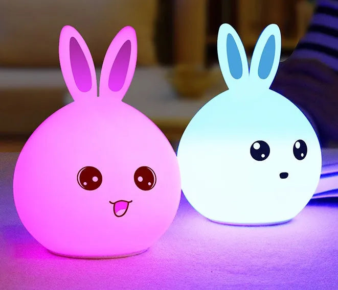 Cute rabbit-shaped night light made of soft silicone with touch sensor, showing seven LED colour options, on a bedside table.