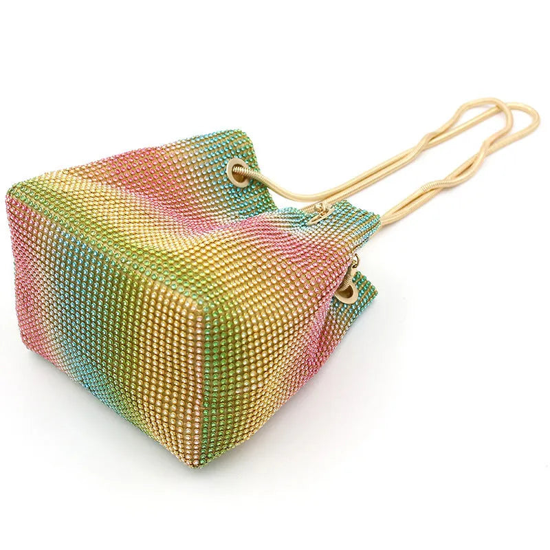 Soft rainbow rhinestone bucket handbag with adjustable long strap on a neutral background.