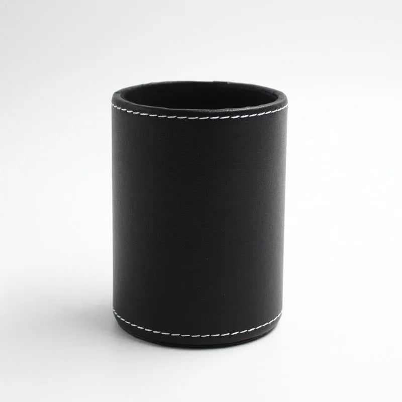 A small, round black leather pen holder standing on a wooden desk.