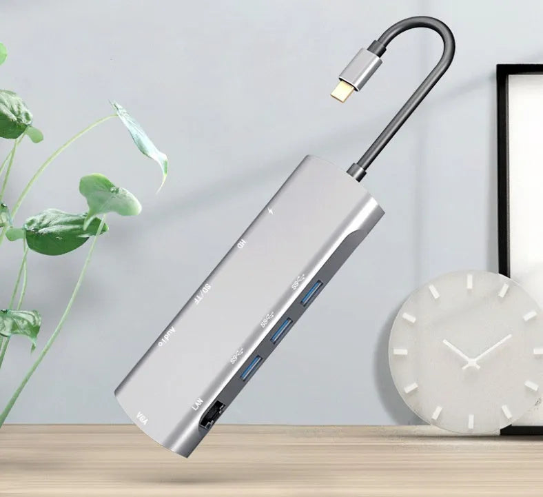Grey aluminium USB-C docking station with HDMI, VGA, USB 3.0, and PD charge ports on a desk.