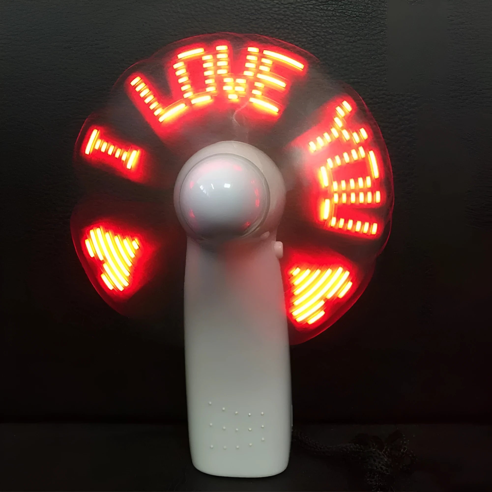 White handheld mini fan with LED lights displaying a love heart pattern, shown next to AAA batteries for scale.