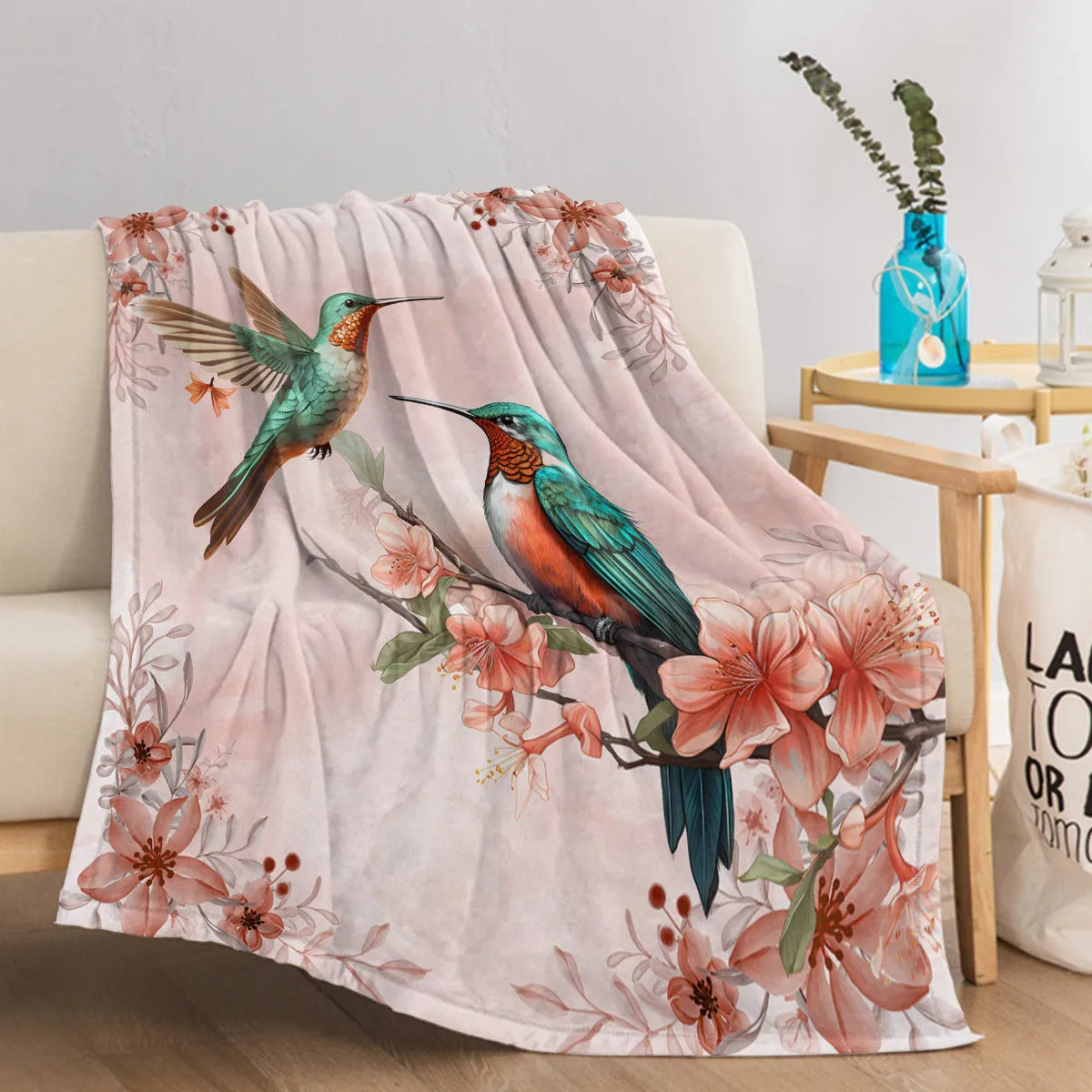 Pink hummingbird floral fleece throw blanket made of soft flannel velvet, folded on a sofa