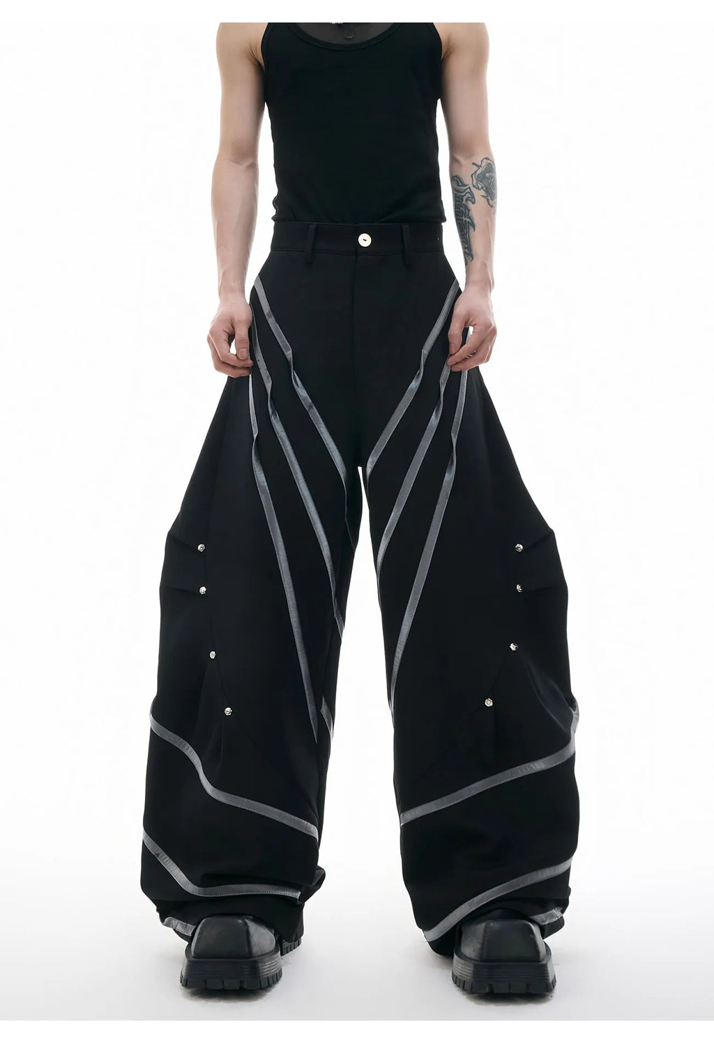 Men's black trousers with pleated detail and metal rivets, showing three-dimensional cut.