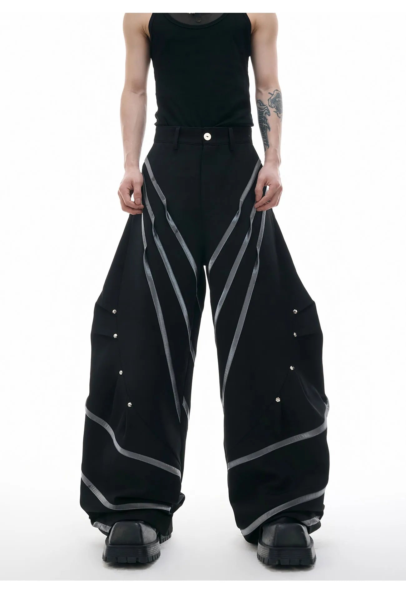 Men's black trousers with pleated detail and metal rivets, showing three-dimensional cut.