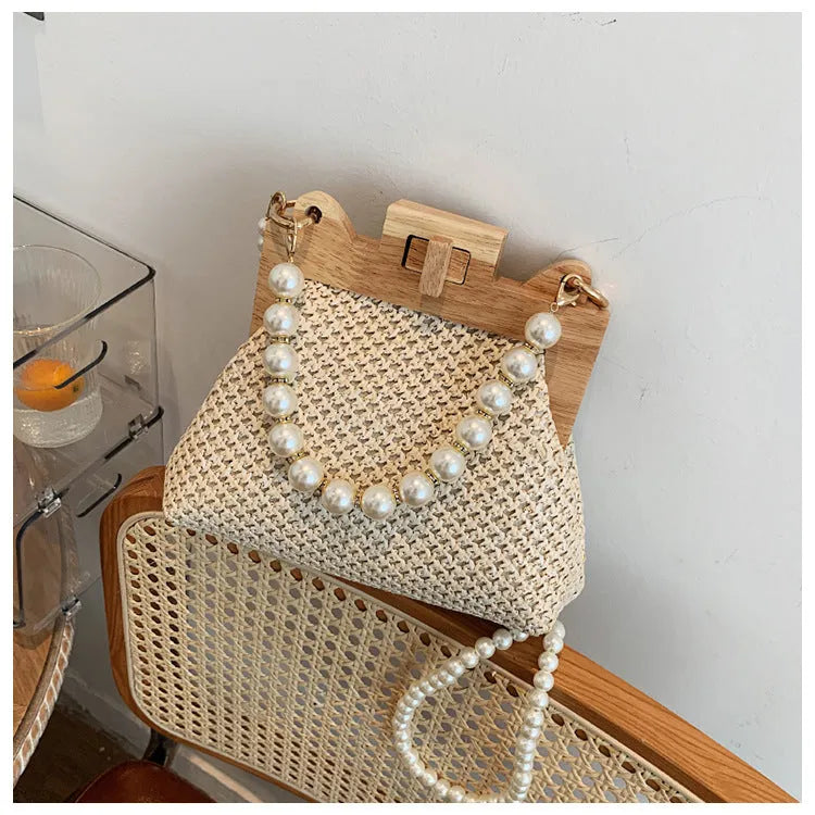 Women's woven straw shoulder bag with pearl chain detail showing horizontal square shape and multiple internal pockets