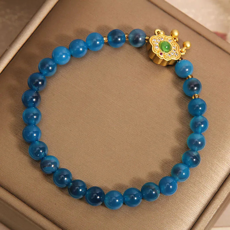 Blue sugar heart agate safety lock pendant on women's bracelet with alloy inlay and crystal accents.